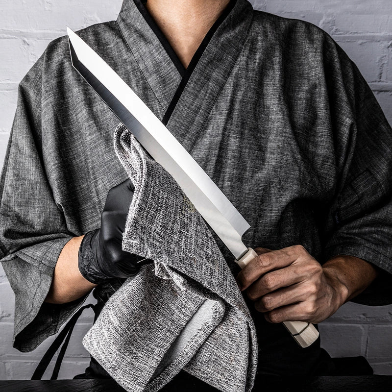 Person in traditional attire holding a large knife with a gray background