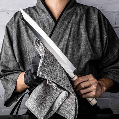Person in traditional attire holding a large knife with a gray background